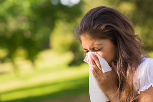 person in a park, sneezing into tissue
