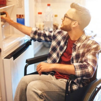 Young man in wheelchair getting item out of refrigerator